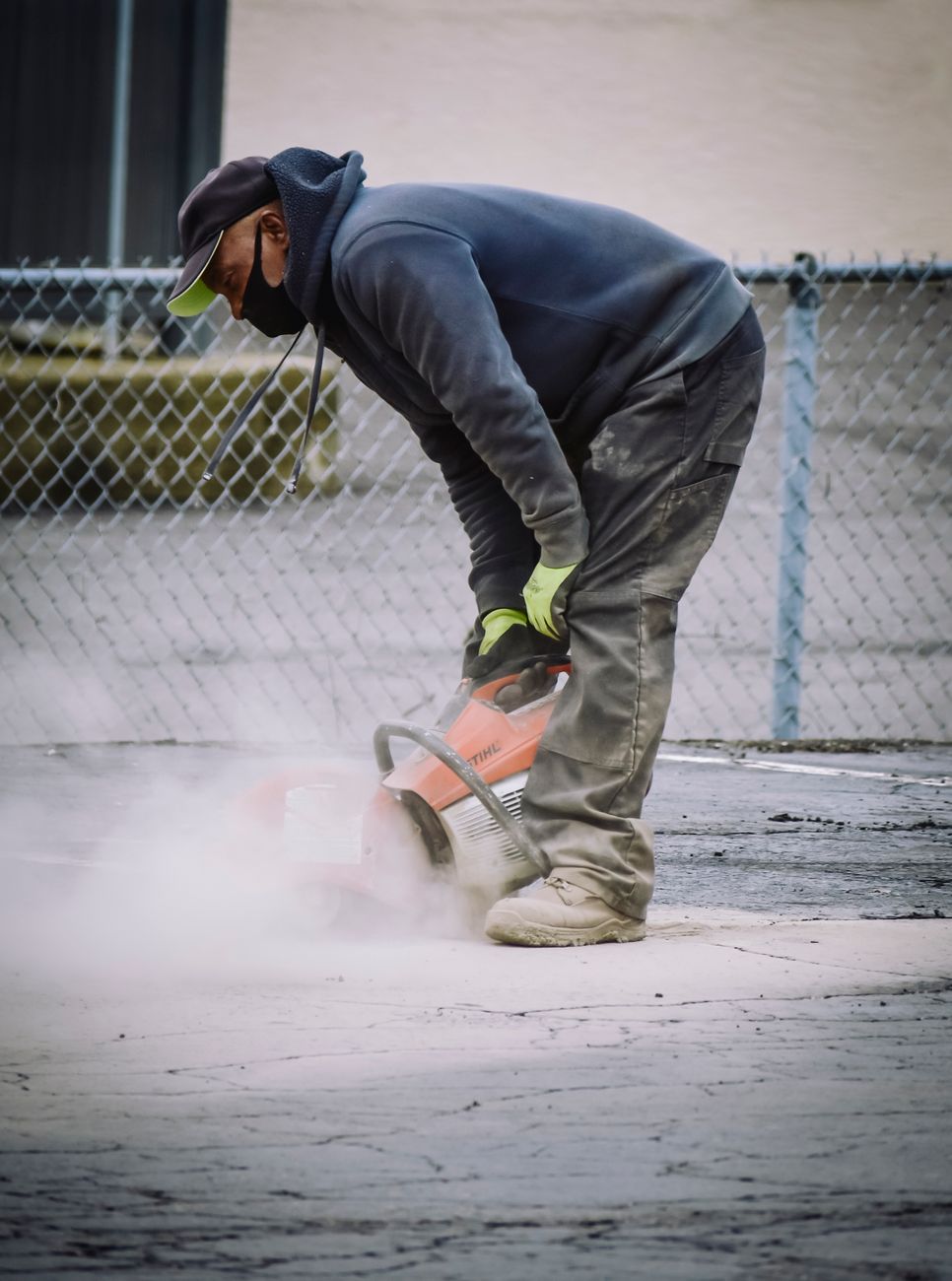 A construction worker in safety gear cutting concrete on an outdoor pavement